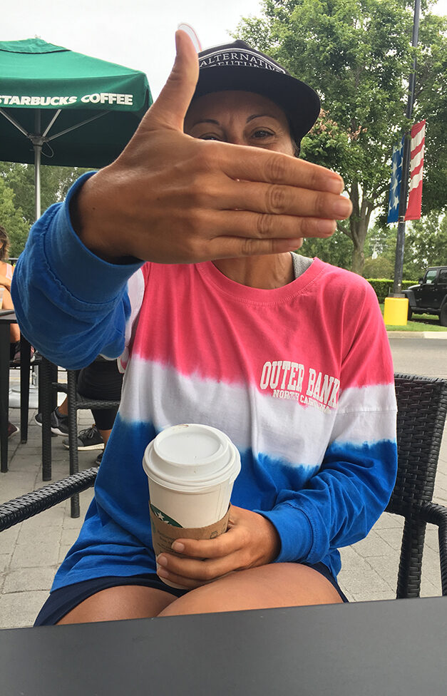 An image of Karen sitting on the patio of a coffee shop with her hand covering her face. Use our Trusted Housesitters discount code to get 25% off!