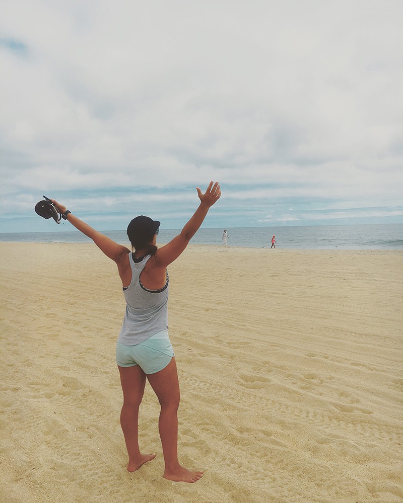 A picture of Karen from behind on the beach in South Carolina. She has her hands in the air and is feeling grateful for Trusted Housesitters!