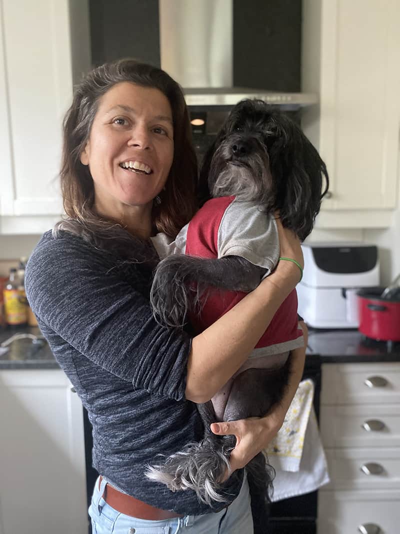 A picture of Donna holding Banjo, a crestipo dog breed. Banjo is wearing a shirt because he has no hair on his body.