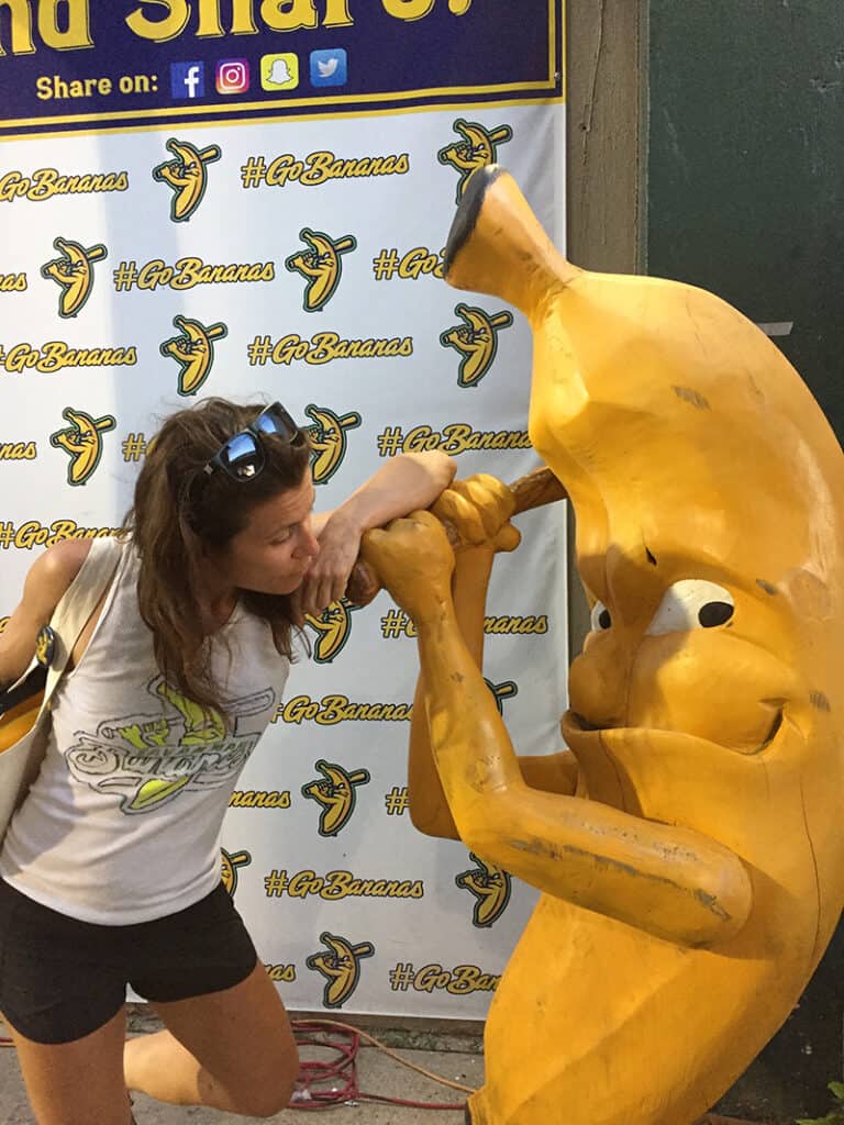 Donna posing beside a carving of a banana holding a baseball at the Savannah Banana's baseball game.