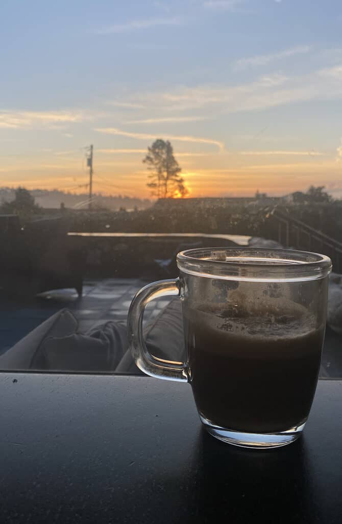 A picture of a clear mug of coffee overlooking a beautiful sunrise.